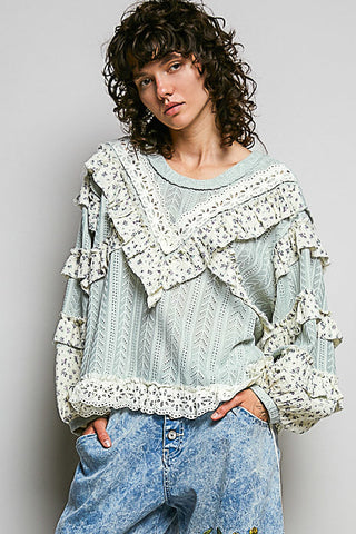 Person wearing a light blue embroidered pants and a matching top with ruffled details on a plain background