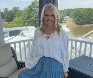 Woman in a white blouse and blue skirt sitting on a porch with a scenic background.