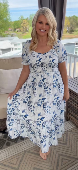 Woman wearing a floral dress sitting on a porch with a scenic background
