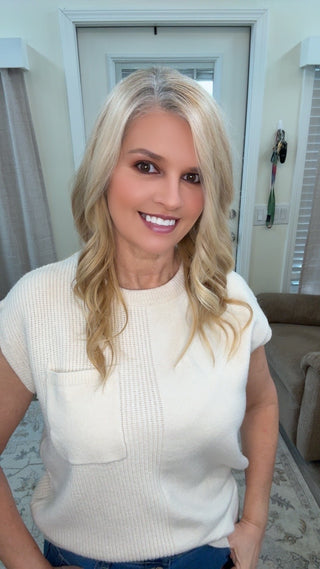 Woman with blonde hair wearing a white sleeveless top in a living room setting.