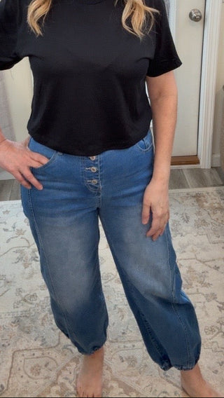 Woman wearing a black t-shirt and blue jeans standing in a living room.