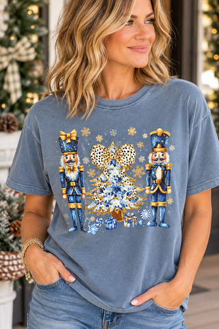 Blue garment-dyed Christmas T-shirt with blue-and-gold nutcrackers, a floral Christmas tree, leopard-print bow, snowflakes, and presents.