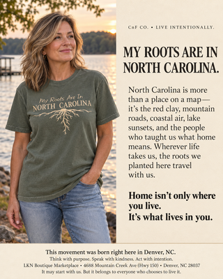 A woman wearing an olive green graphic t-shirt with 'My Roots Are In North Carolina' printed on the front, standing outdoors near a body of water. The image is split into two columns: the left shows the model wearing the shirt, and the right features a beige text block with promotional copy for LKN Boutique.