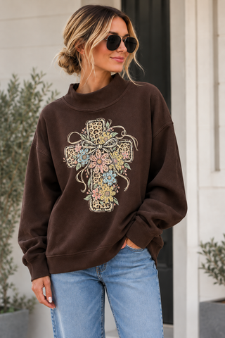 Chocolate brown oversized mock neck sweatshirt with a leopard-print cross, pastel flowers, and bow details, styled with jeans.