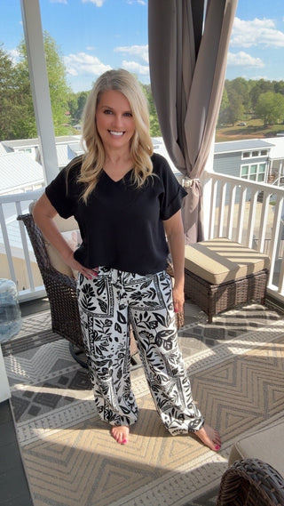 Woman wearing a black t-shirt and patterned pants standing on a patio.